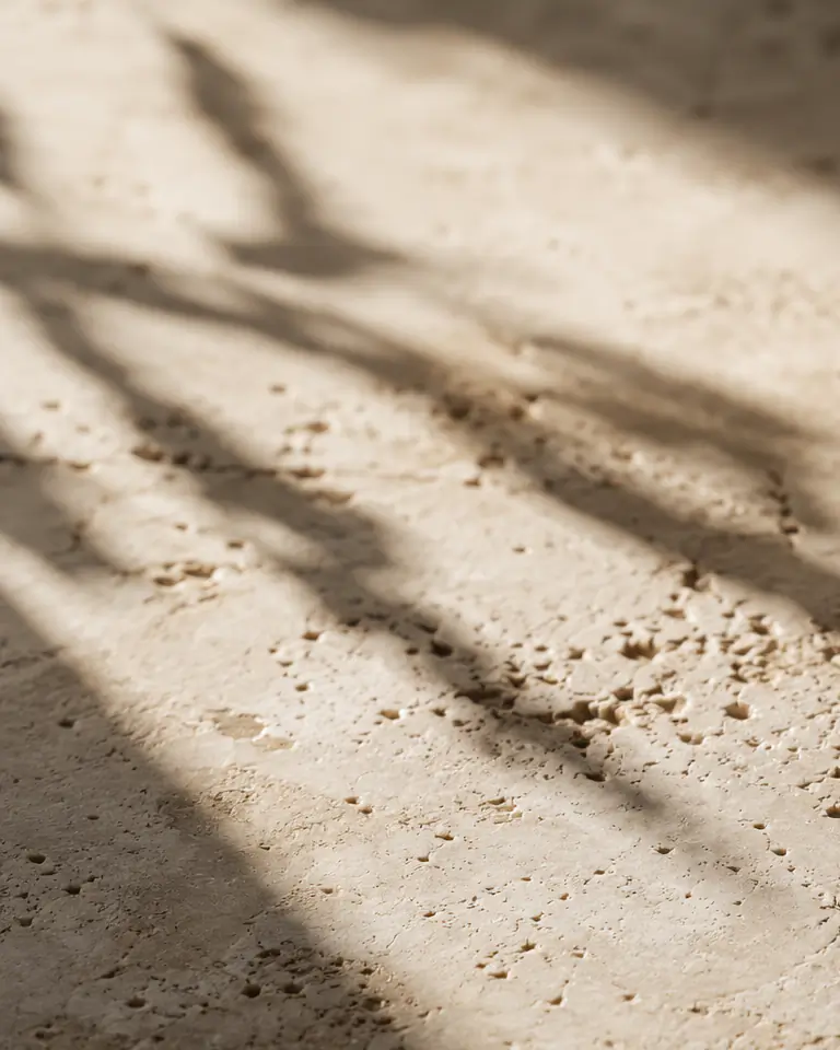Sunlit travertine crossed by soft, diagonal leaf shadows.